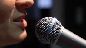 Close-up of mouth and lips of woman singing or speaking into microphone. She is standing on black background with microphone in front of her mouth. Concert or recording studio. - Powered by Shutterstock - Get 15% off with code: PIKWIZARD15