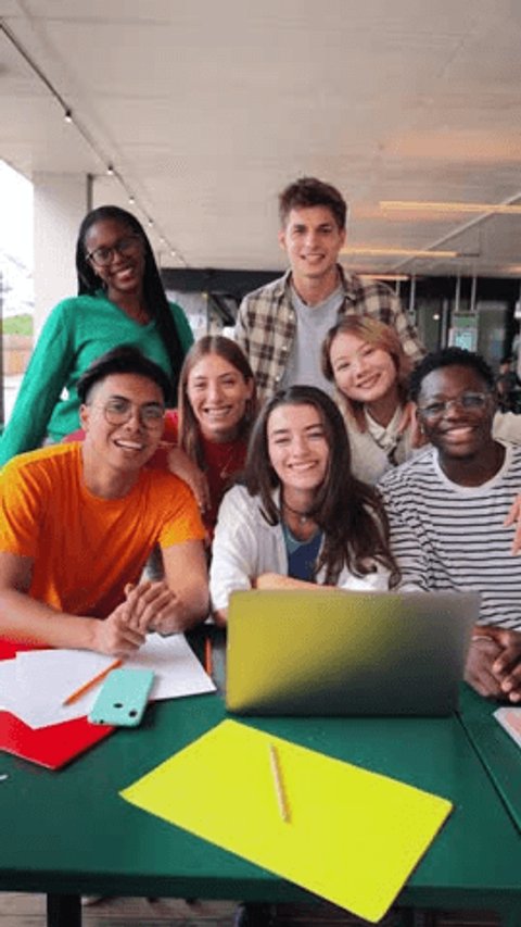 Vertical portrait. Group of young teenage students waving hands at library, using a laptop, looking at camera. Happy classmates studying and doing homeworks at highschool. Multiracial academy people Video de stock