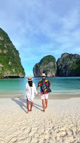 A couple strolls along the sandy beach, the woman's hand in the mans, as they enjoy the view of the water, sky, and natural landscape around them. Maya Bay, Koh Phi Phi, Thailand Royalty-Free Stock Footage #3447767141