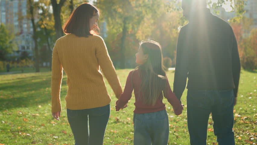 Happy Caucasian family holding hands walking in park talking parents with child talk speaking conversation walk in city outdoors nature weekend holiday spend time together sunny weather autumn spring