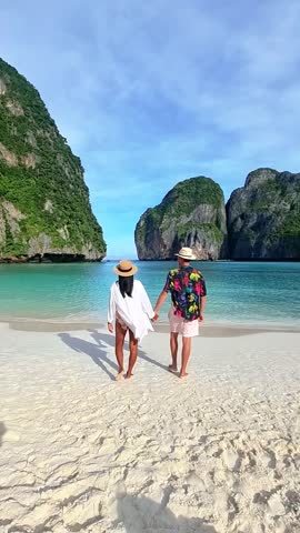 A couple strolls on the beach, palms intertwined, as the azure sky meets the shimmering water. A picturesque natural landscape with mountains in the distance Maya Bay, Koh Phi Phi, Thailand