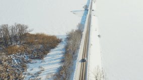 Aerial shot of car riding through snow covered road near frozen lake. White SUV driving at dam route on winter day. Flying over the auto moving through bridge of river. Scenic landscape way. Top view - Powered by Shutterstock - Get 15% off with code: PIKWIZARD15