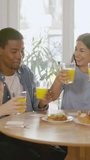 Happy multiethnic friends toasting with juice during breakfast at home