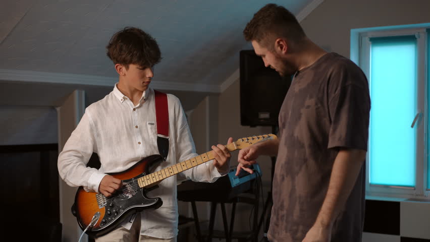 Slow motion. A young guitarist plays an electric guitar and listens to the instructions of his mentor, during a rehearsal at a music school Royalty-Free Stock Footage #3447814181