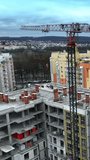 Construction cranes towering above the house in construction. Beautiful residential area full of modern apartment blocks. Cityscape at the background. Vertical video.