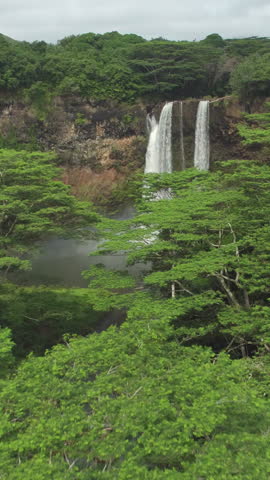 AERIAL: Flying towards a spectacular waterfall in the middle of an untouched rainforest in the heart of Kauai island. Cinematic drone point of view of a breathtaking waterfall in lush green Hawaii.