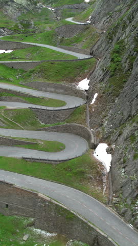 AERIAL: Cinematic aerial view of a hairpin road snaking up a mountain in Switzerland. Tourists in white car stop to observe the picturesque Swiss Alps during a fun road trip across Passo San Gottardo. Royalty-Free Stock Footage #3447877155