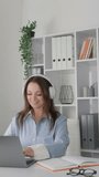 In this vertical video, a young entrepreneur uses a laptop to plan her business and communicate with customers over the internet. She is focused on growing her startup by studying the market and