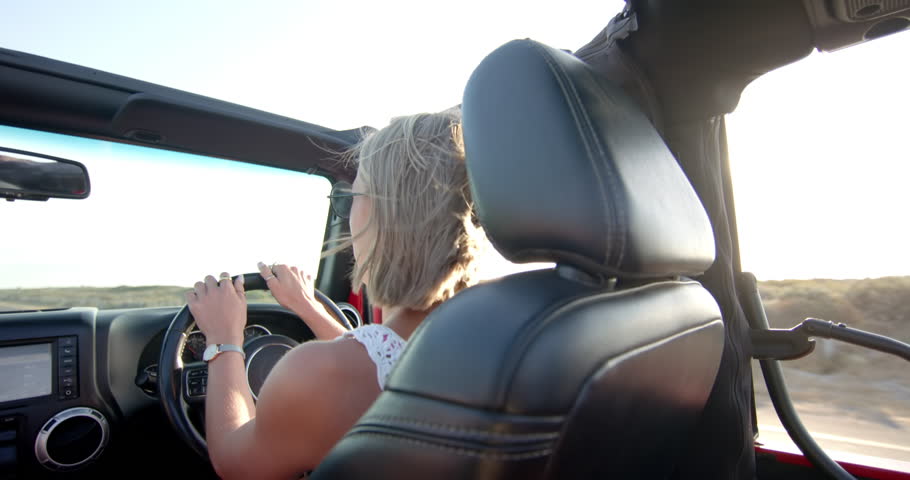 Young Caucasian woman enjoys a sunny drive in a convertible on a road trip. Her joyful expression suggests a sense of freedom and adventure on the open road, slow motion. Royalty-Free Stock Footage #3447945643