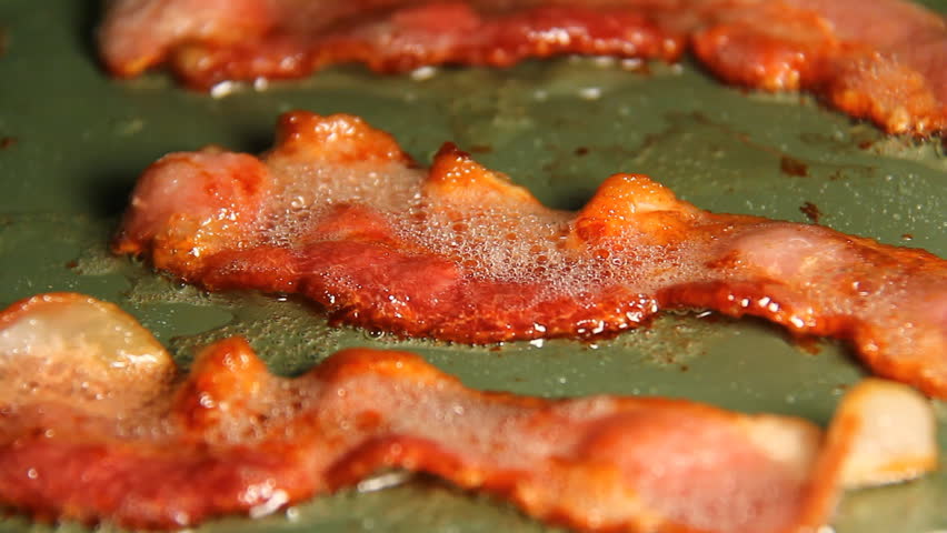 Bacon 4. Three strips of bacon frying in a pan turned over with tongs. Later in