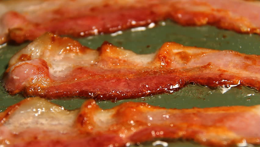 Bacon 2. Three strips of bacon frying in a pan.
