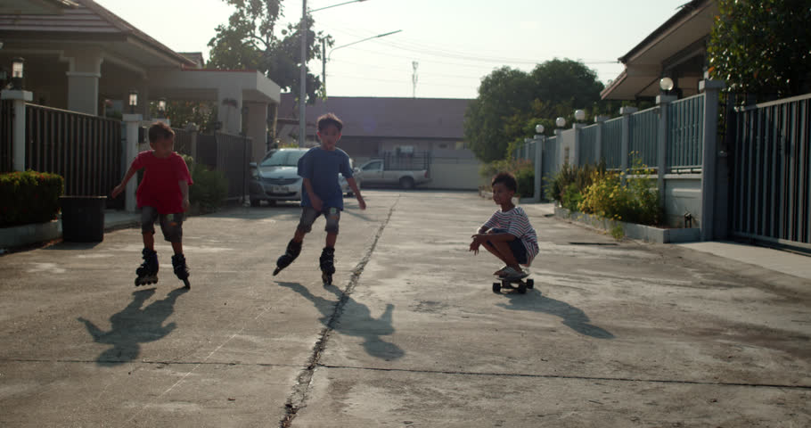 A group of elementary school-age Asian boys, the children of neighbors, had fun rollerblading and skateboarding on the village streets in the evening after returning from school.