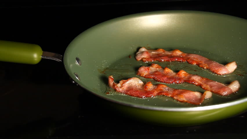 Bacon 3. Three strips of bacon frying in a pan.