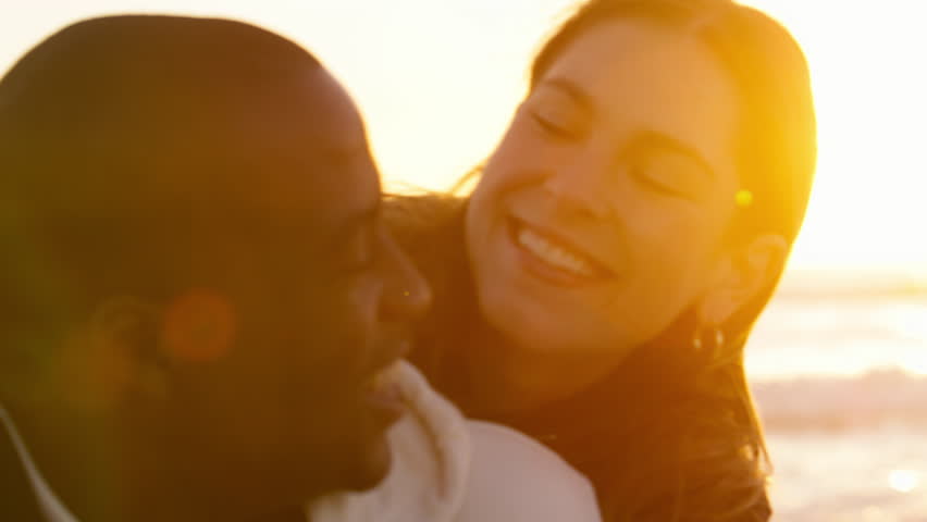 Shot of casually dressed loving young couple sitting on sand hugging watching beautiful sunrise morning over beach and sea in South Africa with lens flare - shot in slow motion