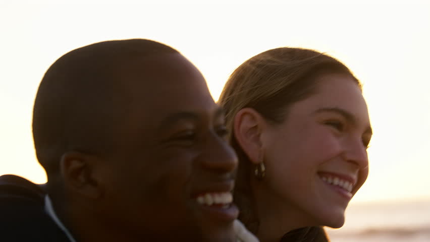 Shot of casually dressed loving young couple sitting on sand hugging watching beautiful sunrise morning over beach and sea in South Africa with lens flare - shot in slow motion
