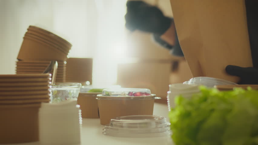 Using paper bags and containers, a volunteer packs food into biodegradable containers in a modern industrial kitchen. An organization of volunteers is actively distributing food Royalty-Free Stock Footage #3448081133