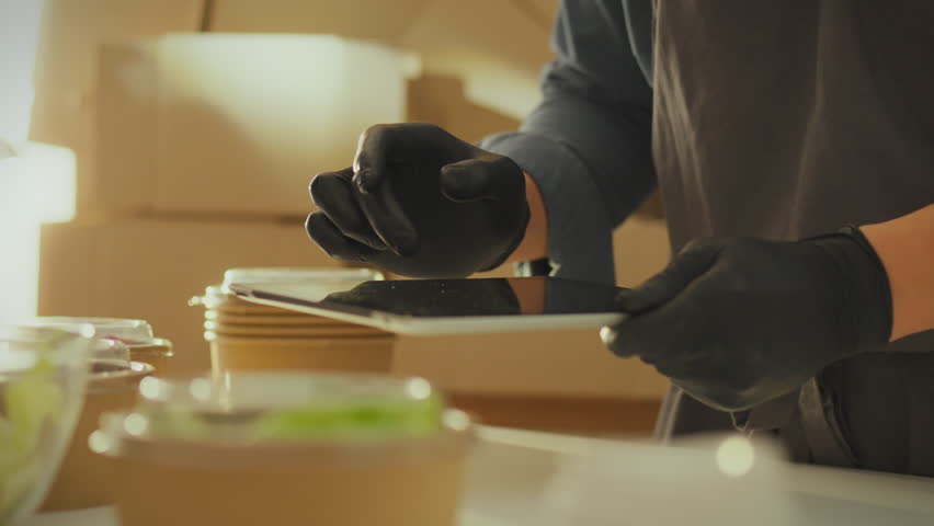 Against the backdrop of boxes of groceries, a warehouse manager, working with a touchscreen tablet, carefully analyzes information on food orders. A tablet in his hands to control current accounting