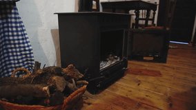 Slow motion Caucasian bearded man sits by the fireplace and puts firewood into a metal burning stove, making fire for heating the cozy room in rustic house. Countryside lifestyle. People and energy