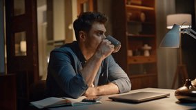 Overworked man drinking tea at cozy night workplace closeup. Serious tired guy looking distance enjoying coffee cup at evening apartment. Remote worker sipping hot beverage relaxing alone at late home - Powered by Shutterstock - Get 15% off with code: PIKWIZARD15