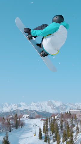 SLOW MOTION: Male snowboarder soars through the air and does a breathtaking trick. Spectacular shot of a snowboarding pro doing a rotating grab stunt while training in ski resort snowpark.