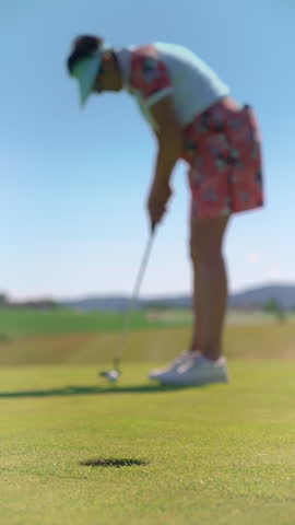 Mature woman playing golf. Golfer hitting golf shot and hammering a ball into the golf hole. Beautiful sunny landscape, with green hills and blue sky.