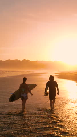 AERIAL SILHOUETTE: Two surfers carrying surfboards and checking waves after surf session. Surf friends walking on the beach in golden light. Gorgeous summer scenery at Playa Venao in Panama. Royalty-Free Stock Footage #3448201513