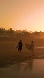 AERIAL SILHOUETTE: Two surfers walking down the beach carrying surfboards. Surf couple chatting in golden light before morning surf session. Gorgeous summer scenery at Playa Venao in Panama.