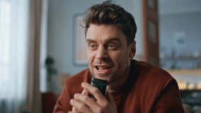 Smiling man singing remote controller as microphone sitting modern living room close up. Happy guy dancing along rhythmic music having fun at home alone. Funny hipster enjoy favorite song in apartment - Powered by Shutterstock - Get 15% off with code: PIKWIZARD15