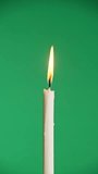 Vertical one candle burns on a green background. Candle flame on chroma key. Copy space. Fire flame of candlelight close-up. Alpha channel background. Isolated. Concept holiday, religious, memories 4K