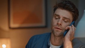 Worried man talking smartphone in dark modern apartment closeup. Frowning guy having serious telephone conversation sitting home table. Unshaven freelancer discussing problem by mobile phone call - Powered by Shutterstock - Get 15% off with code: PIKWIZARD15