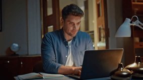 Smiling businessman browsing computer texting email at cozy dark flat closeup. Happy relaxed man looking laptop screen chatting social networks at home. Positive handsome guy typing keyboard at house - Powered by Shutterstock - Get 15% off with code: PIKWIZARD15