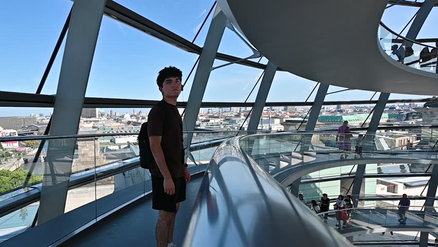 Berlin,Germany,August 15,2023. Beautiful slow motion footage with a young man looking inside the glass and metal dome located on the roof of the Reichstag building. In the background other people.