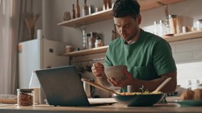 Focused man having breakfast reading laptop at kitchen closeup. Unshaven serious guy eating granola looking at window at modern light home. Calm freelancer taking lunch spending time at house alone - Powered by Shutterstock - Get 15% off with code: PIKWIZARD15