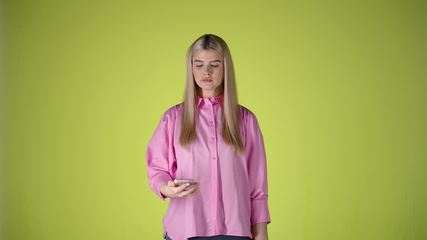Cucasian woman looks at her cellphone amazed and surprised mobile studio blonde girl shot with technology, reading screen, infinite background isolated shot