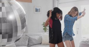 Animation of mirror ball over two diverse teenage girls having fun dancing at home. Friendship, youth, music, fun, weekend and lifestyle, digitally generated video.