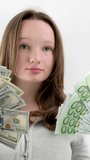 golden youth teenage girl with two large packs of new banknotes 100 dollar bills 100 euro bills on a white background in a sports gray sweater. loose hair young confident girl. New generation