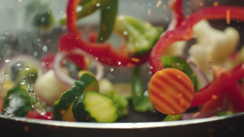 Closeup of chef preparing and throwing vegetable mix on frying pan on fire. Preparation fresh appetizing food. Vegetables flying into the pan in slow motion. Healthy vegetarian food cooking close-up