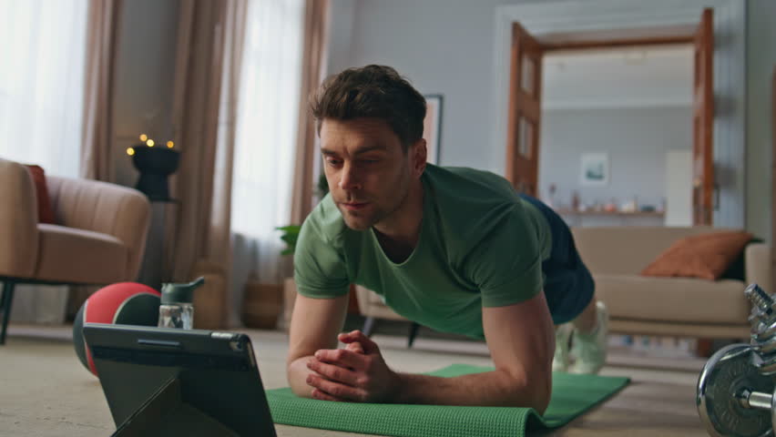 Sportsman watching workout tutorial video by tablet training at home closeup. Focused strong man looking computer screen following guide of online lesson. Fit athlete doing plank exercise in apartment Royalty-Free Stock Footage #3448308607