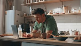Domestic businessman watching laptop at morning kitchen closeup. Focused man eating granola reading email at cozy interior. Unshaven serious guy tasting cornflakes feeling concentrated at apartment - Powered by Shutterstock - Get 15% off with code: PIKWIZARD15