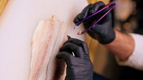 vertical video close-up of cook in a professional kitchen in a white jacket using tweezers to remove bones from a fish