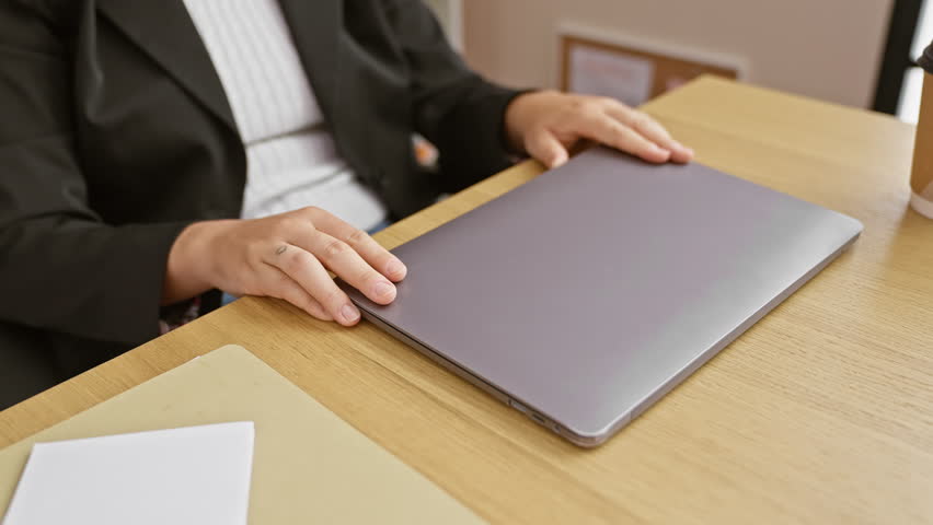 A young hispanic woman with curly hair works on her laptop at an office desk.