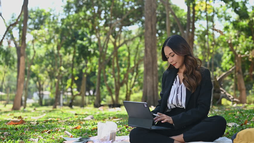 Attractive businesswoman working remotely outside office drinking coffee and using digital tablet
