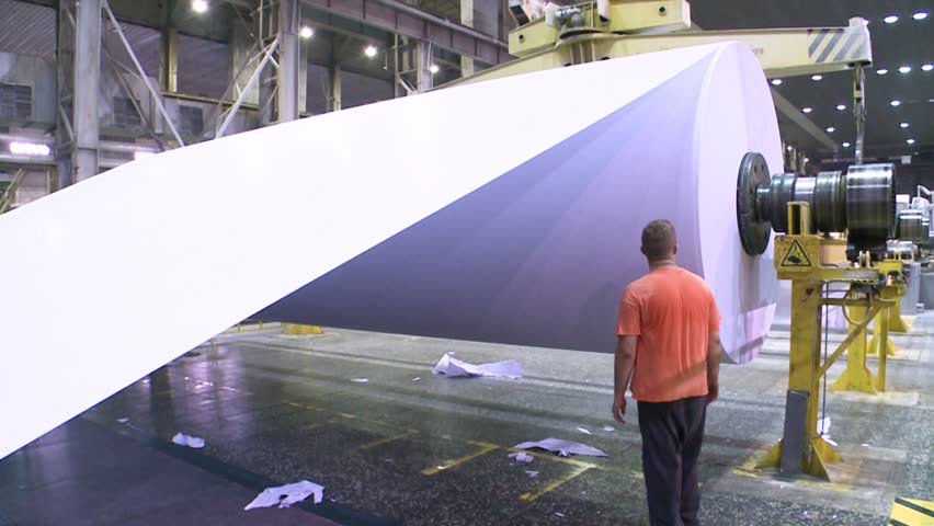 Workers closing a roll of paper on a paper machine. Paper production.