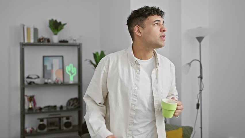 A young man enjoys his morning coffee in a modern living room, exuding casual comfort and a relaxed homey ambiance.