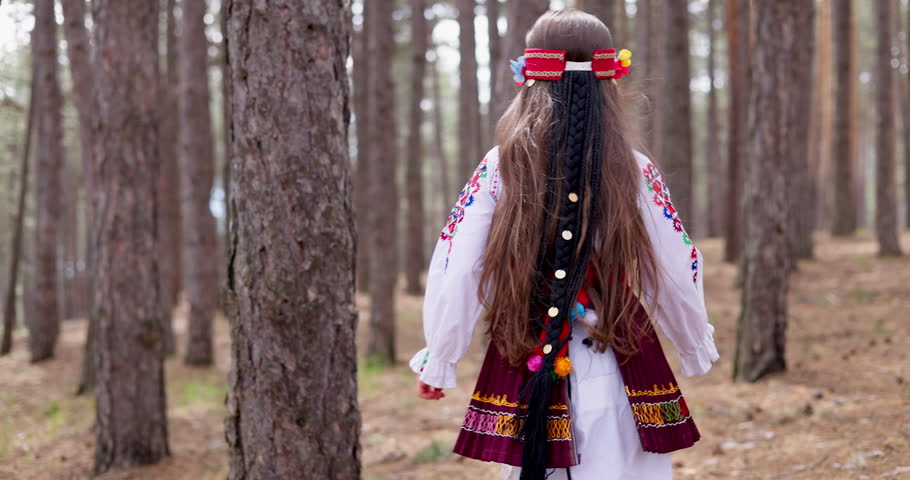 Bulgarian woman beautiful girl in ethnic folklore costume walking between old trees in mountain deep forest, Bulgaria