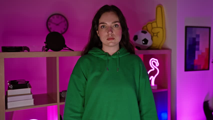 A confident young woman stands arms crossed in a neon-lit gaming room at night, exuding a cool and trendy vibe.