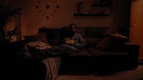 Front view of a young Caucasian man having fun and laughing watching TV while lying on the sofa at home at night eating popcorn. Male enjoying a movie in the living room in the dark. - Powered by Shutterstock - Get 15% off with code: PIKWIZARD15