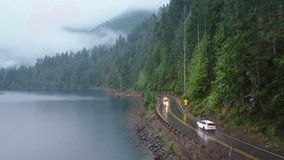 Cinematic evergreen forest Olympic National park. Travelers in rainforest Washington. Road trip concept aerial. SUV car with tourists driving by scenic route along beautiful lake Crescent on rainy day - Powered by Shutterstock - Get 15% off with code: PIKWIZARD15