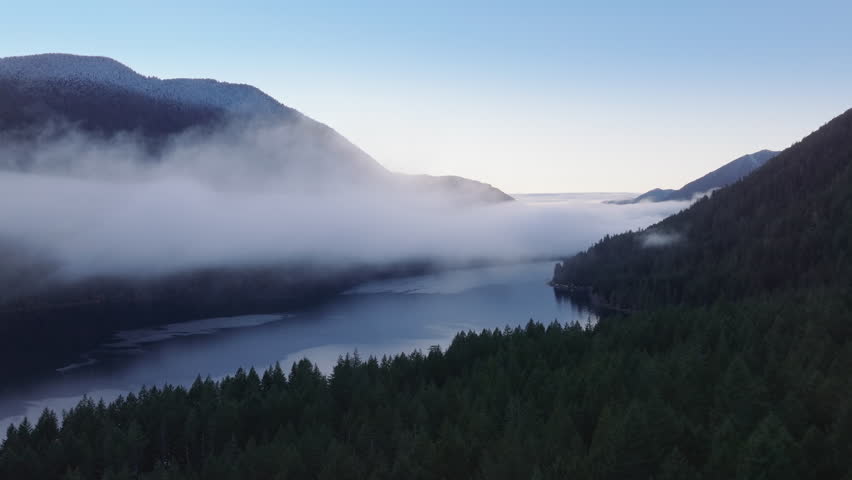 Olympic National park landscape on frosty winter evening. Scenic Washington nature with foggy rainforest. Lake Crescent aerial at twilight. Cinematic cloud mist flying above mirror like mountain lake