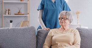 Smiling friendly health care worker or caregiver talking with elderly woman and hugging. Portrait of a young female nurse with her senior happy patient sitting in nursing home. 4k video.